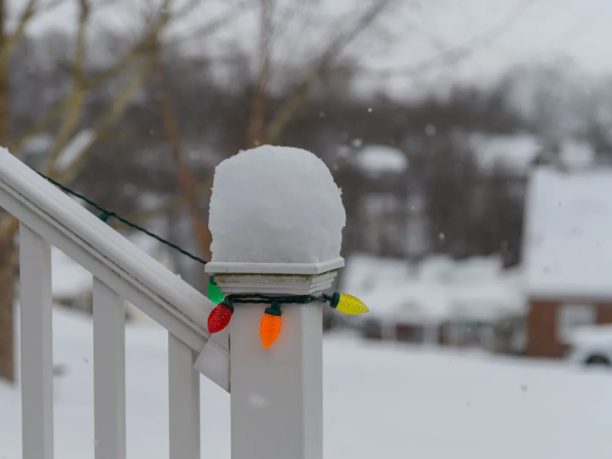 Red, green, orange, and yellow holiday bulbs on a snow-capped porch railing.