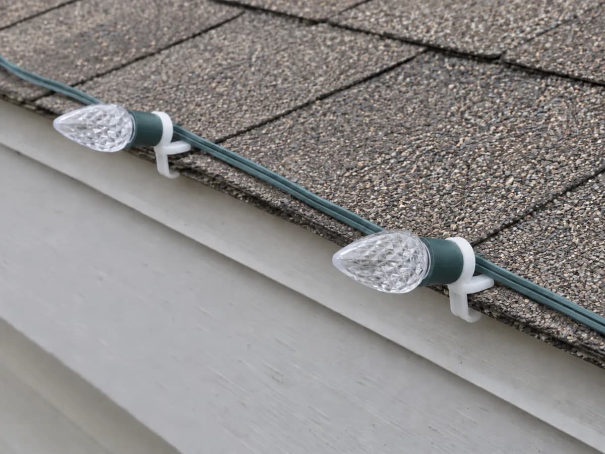 Illustration of clear C9 bulbs in green sockets held at a roof edge by compact white shingle clips.